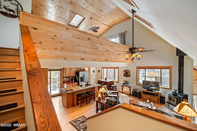 living area featuring stairs, a wood stove, high vaulted ceiling, light wood-type flooring, and ceiling fan
