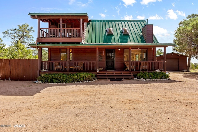 view of front of home with a chimney, an outbuilding, fence, metal roof, and covered porch
