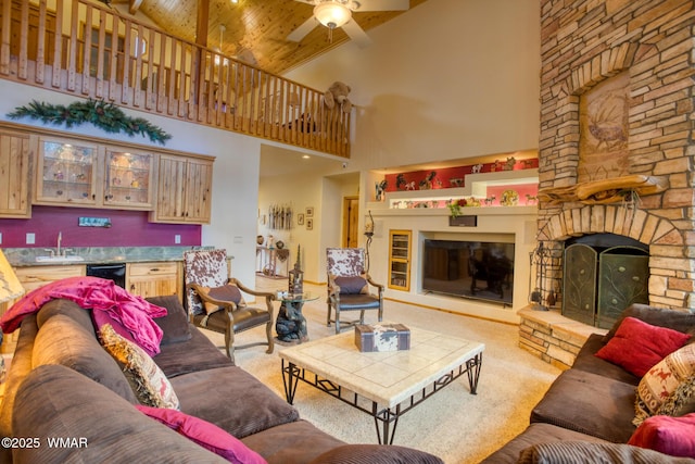 carpeted living room with a sink, a ceiling fan, wooden ceiling, a stone fireplace, and high vaulted ceiling
