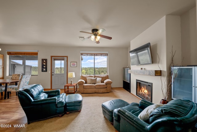 living area with ceiling fan, a glass covered fireplace, and visible vents