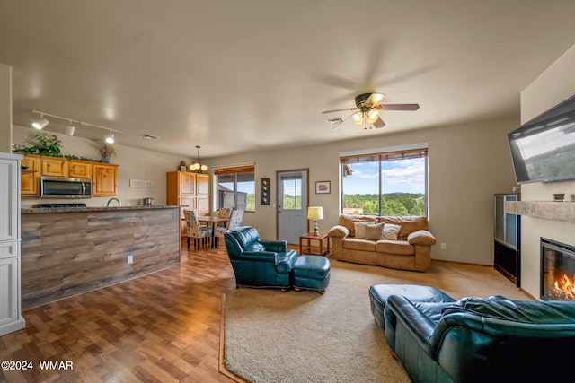 living area featuring light wood finished floors, a glass covered fireplace, a ceiling fan, and rail lighting