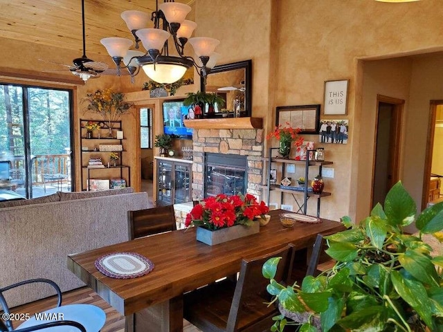 dining area with a fireplace, a high ceiling, and ceiling fan with notable chandelier