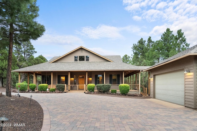 farmhouse with a porch, decorative driveway, roof with shingles, and a garage