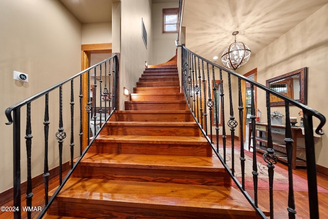 stairway featuring wood finished floors and a notable chandelier