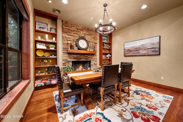 dining room featuring an inviting chandelier, visible vents, wood finished floors, and a stone fireplace