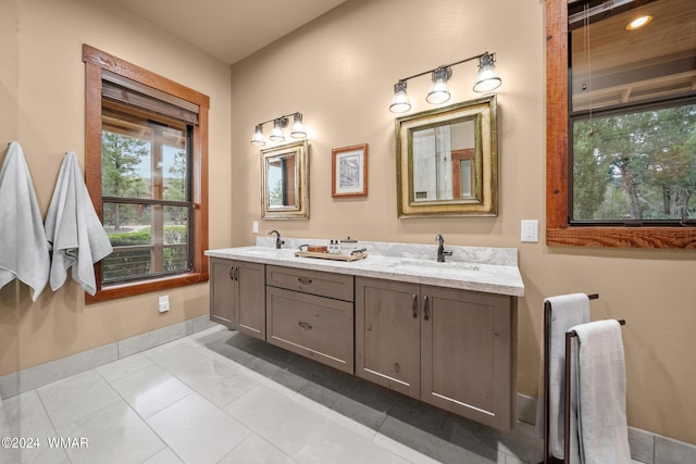 full bath featuring double vanity, tile patterned flooring, baseboards, and a sink