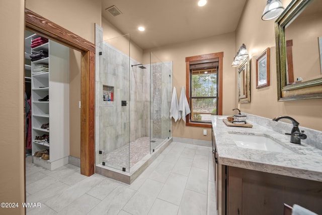 full bathroom featuring double vanity, visible vents, a walk in closet, a shower stall, and a sink