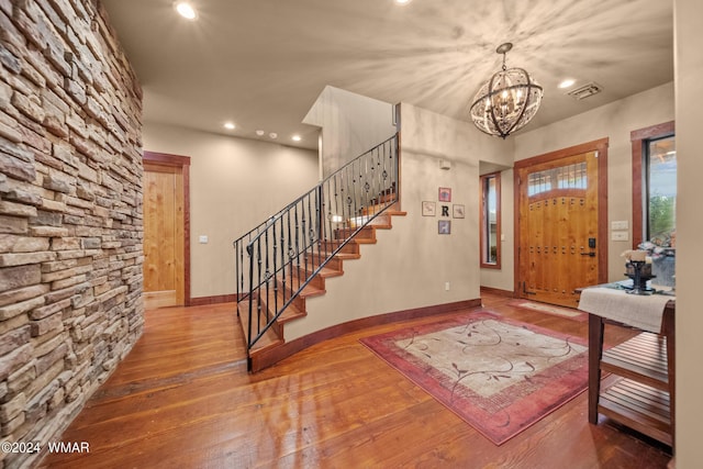 foyer entrance featuring a chandelier, hardwood / wood-style flooring, visible vents, baseboards, and stairs