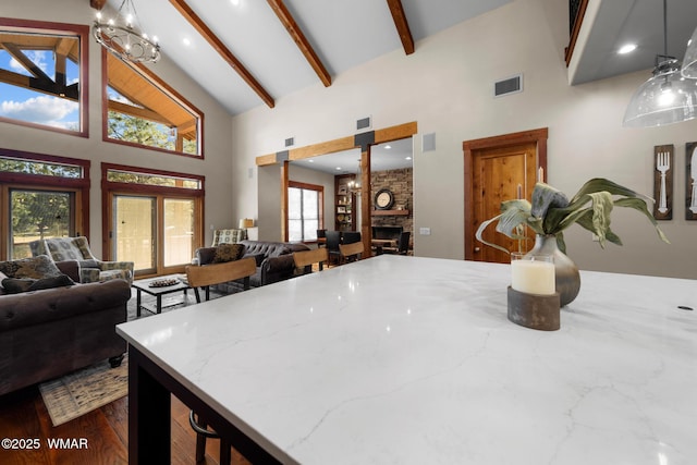 kitchen featuring light stone counters, beam ceiling, visible vents, a stone fireplace, and high vaulted ceiling