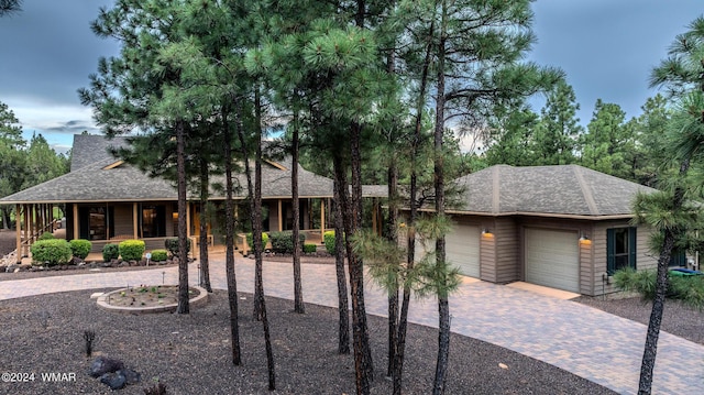 view of front of property featuring a garage, a shingled roof, decorative driveway, and a porch