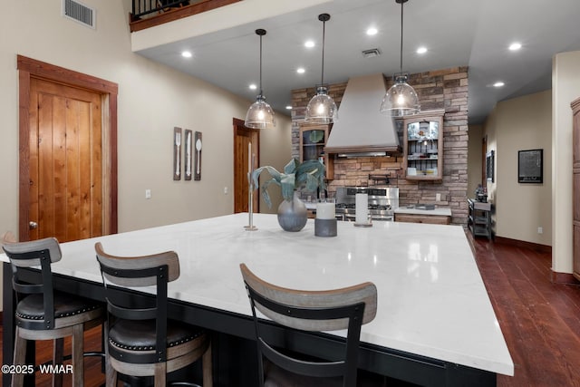 kitchen featuring dark wood-style floors, light countertops, premium range hood, and visible vents