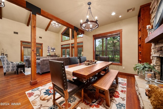 dining space featuring a stone fireplace, beam ceiling, wood finished floors, and visible vents