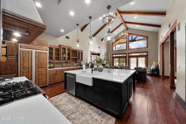 kitchen featuring dark wood finished floors, dark cabinets, beam ceiling, stainless steel dishwasher, and a sink