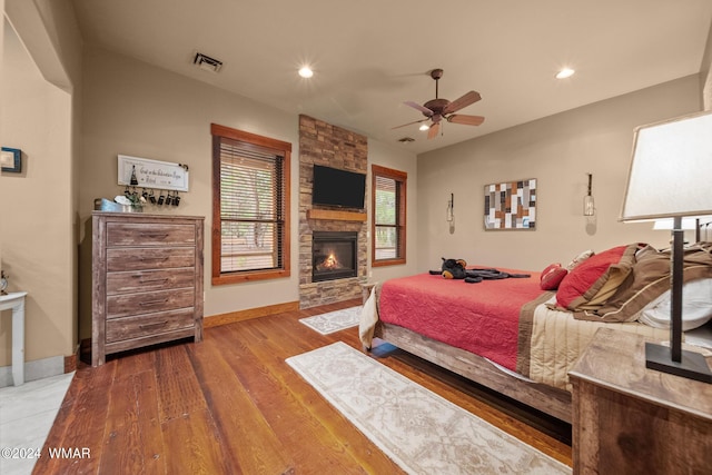 bedroom featuring recessed lighting, a stone fireplace, baseboards, and wood finished floors