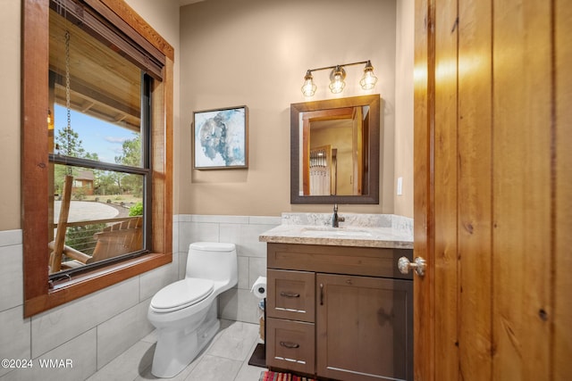 bathroom with a wainscoted wall, tile walls, toilet, vanity, and tile patterned floors