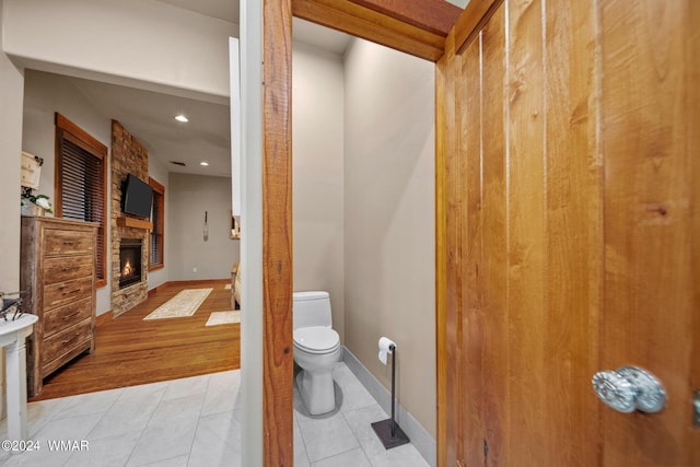 bathroom featuring a stone fireplace, toilet, recessed lighting, baseboards, and tile patterned floors