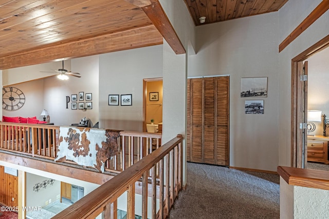 hall with baseboards, lofted ceiling with beams, an upstairs landing, carpet floors, and wood ceiling