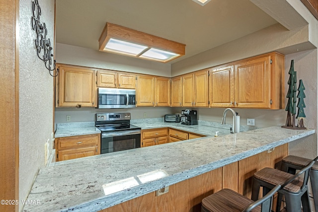 kitchen featuring a sink, a textured wall, a peninsula, stainless steel appliances, and light stone counters