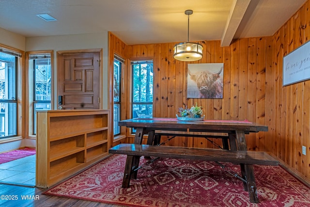 dining space featuring wood finished floors, beamed ceiling, wooden walls, and plenty of natural light