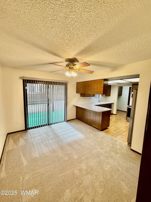 kitchen with light colored carpet, a peninsula, open floor plan, light countertops, and brown cabinetry