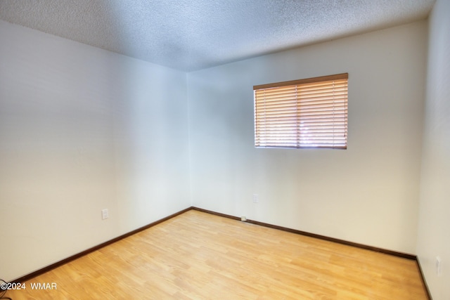 unfurnished room with a textured ceiling, baseboards, and light wood-style floors