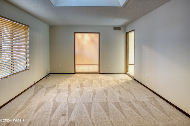 spare room featuring a skylight, baseboards, visible vents, light colored carpet, and a textured ceiling