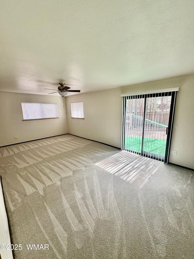 empty room featuring light colored carpet, ceiling fan, a textured ceiling, and baseboards