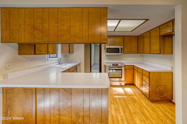 kitchen with appliances with stainless steel finishes, light countertops, a sink, and a peninsula