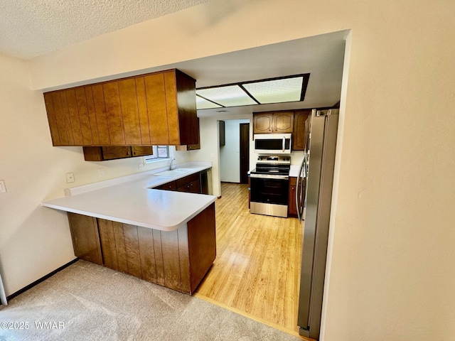 kitchen featuring brown cabinetry, appliances with stainless steel finishes, a peninsula, light countertops, and a sink