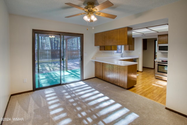 kitchen with white microwave, a peninsula, electric range, light countertops, and brown cabinetry