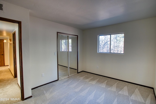 unfurnished bedroom featuring visible vents, baseboards, a closet, and light colored carpet