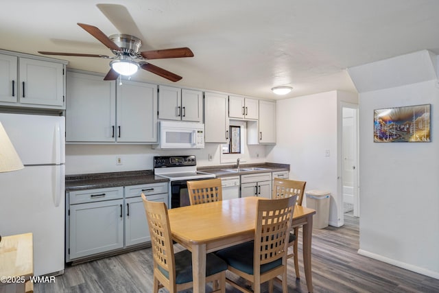 kitchen featuring dark wood finished floors, dark countertops, white appliances, and a sink