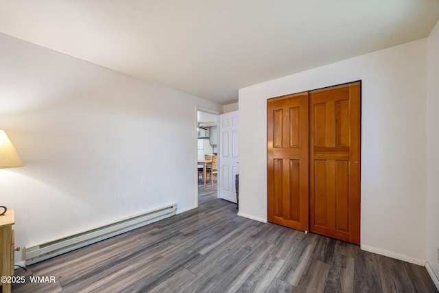 unfurnished bedroom with dark wood-style flooring, baseboard heating, a closet, and baseboards