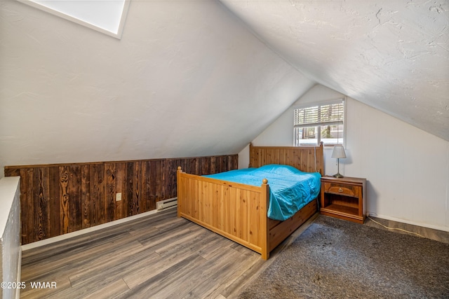 bedroom with a baseboard heating unit, vaulted ceiling, wood walls, and wood finished floors