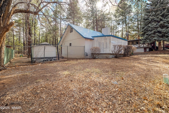 view of property exterior featuring a chimney, fence, and metal roof