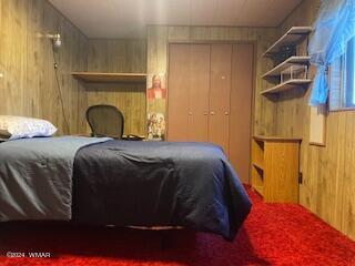 carpeted bedroom with a closet and wood walls