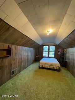 unfurnished bedroom with carpet floors, visible vents, vaulted ceiling, and wooden walls