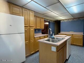 kitchen with white appliances, a kitchen island with sink, light countertops, and a sink