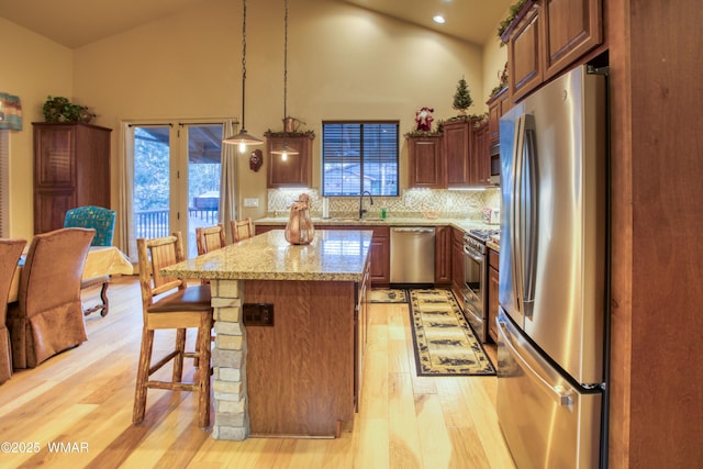 kitchen featuring a kitchen bar, light wood-style flooring, a sink, a kitchen island, and appliances with stainless steel finishes