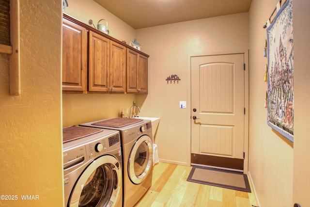 clothes washing area with baseboards, washing machine and dryer, light wood-type flooring, cabinet space, and a sink