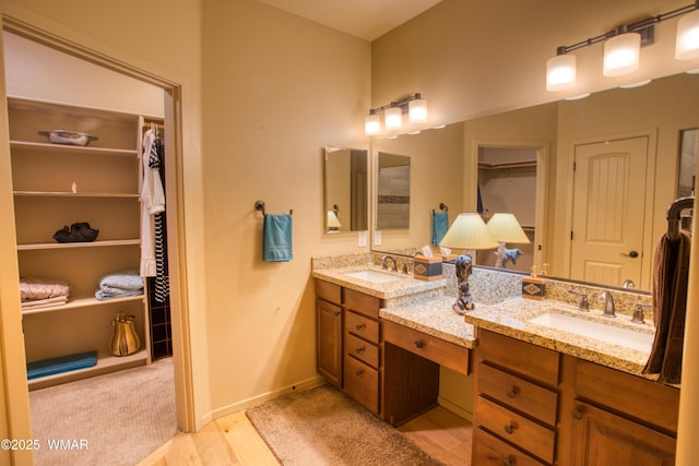 full bathroom with double vanity, a walk in closet, baseboards, and a sink