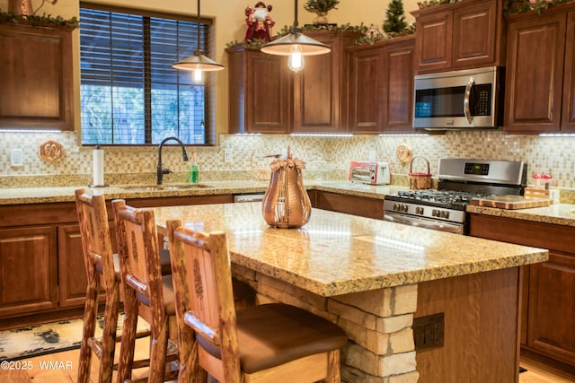 kitchen featuring light stone counters, a sink, stainless steel appliances, a kitchen bar, and backsplash