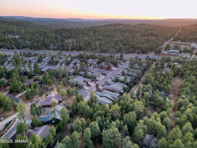 aerial view at dusk featuring a residential view, a mountain view, and a view of trees