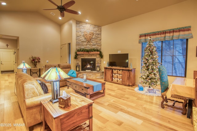 living room featuring light wood finished floors, high vaulted ceiling, recessed lighting, ceiling fan, and a stone fireplace