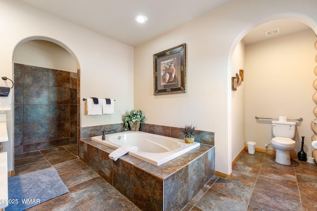bathroom with stone tile floors, visible vents, toilet, and a garden tub