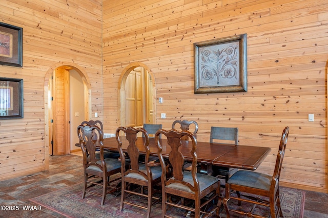 dining room with visible vents, arched walkways, wooden walls, and a towering ceiling