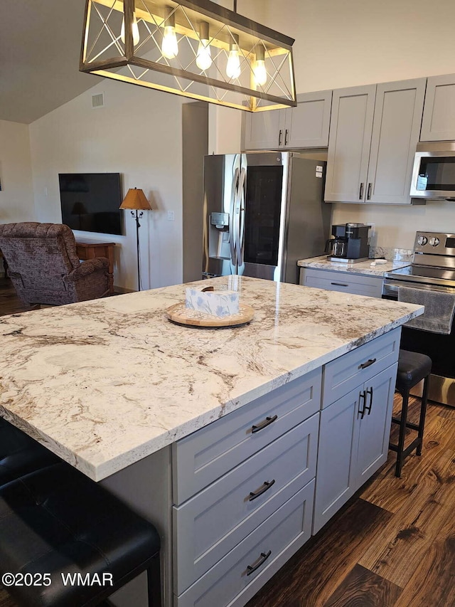 kitchen with light stone counters, stainless steel appliances, a kitchen island, gray cabinetry, and dark wood-style floors