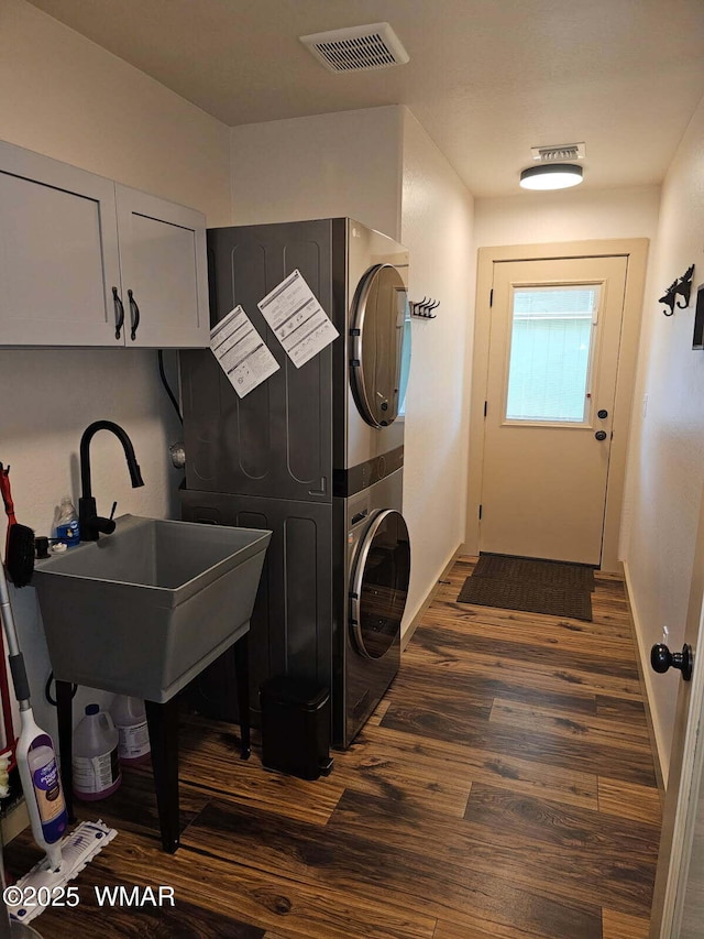 washroom featuring visible vents, baseboards, stacked washing maching and dryer, and dark wood-type flooring