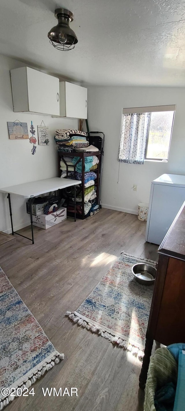 bedroom with light wood-style floors, refrigerator, a textured ceiling, and baseboards