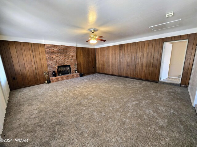 unfurnished living room featuring carpet, a brick fireplace, a ceiling fan, and wooden walls